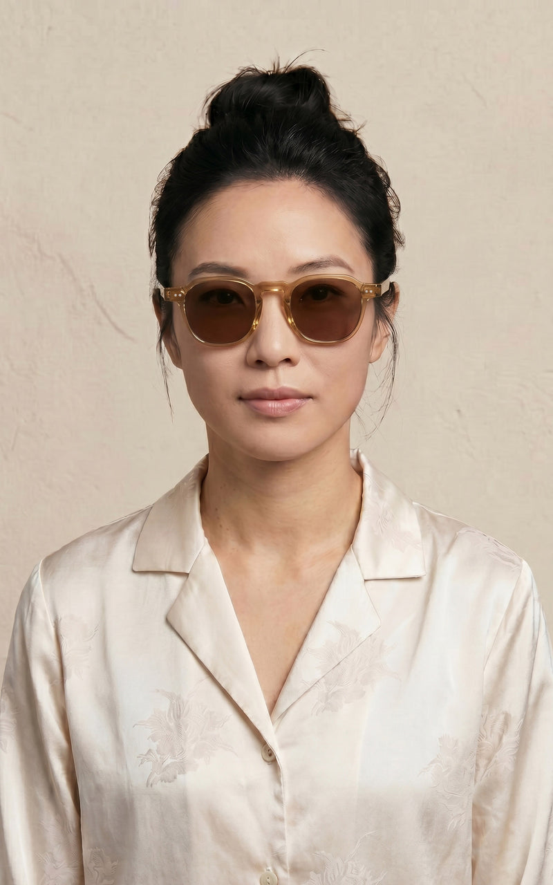 Mulher de óculos de sol com armação redonda clara e camisa bege estampada