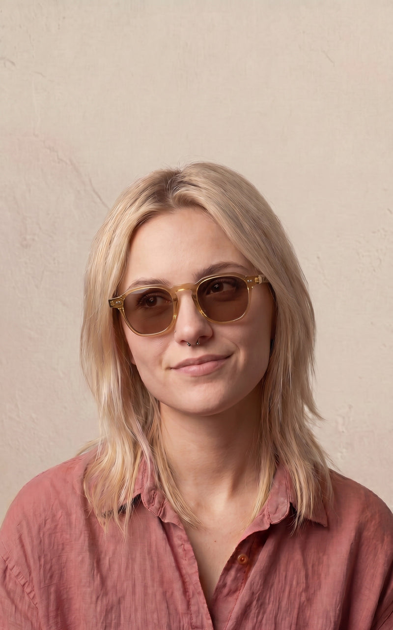 Mulher usando óculos de sol com armação transparente e lentes marrons, vestindo blusa rosa