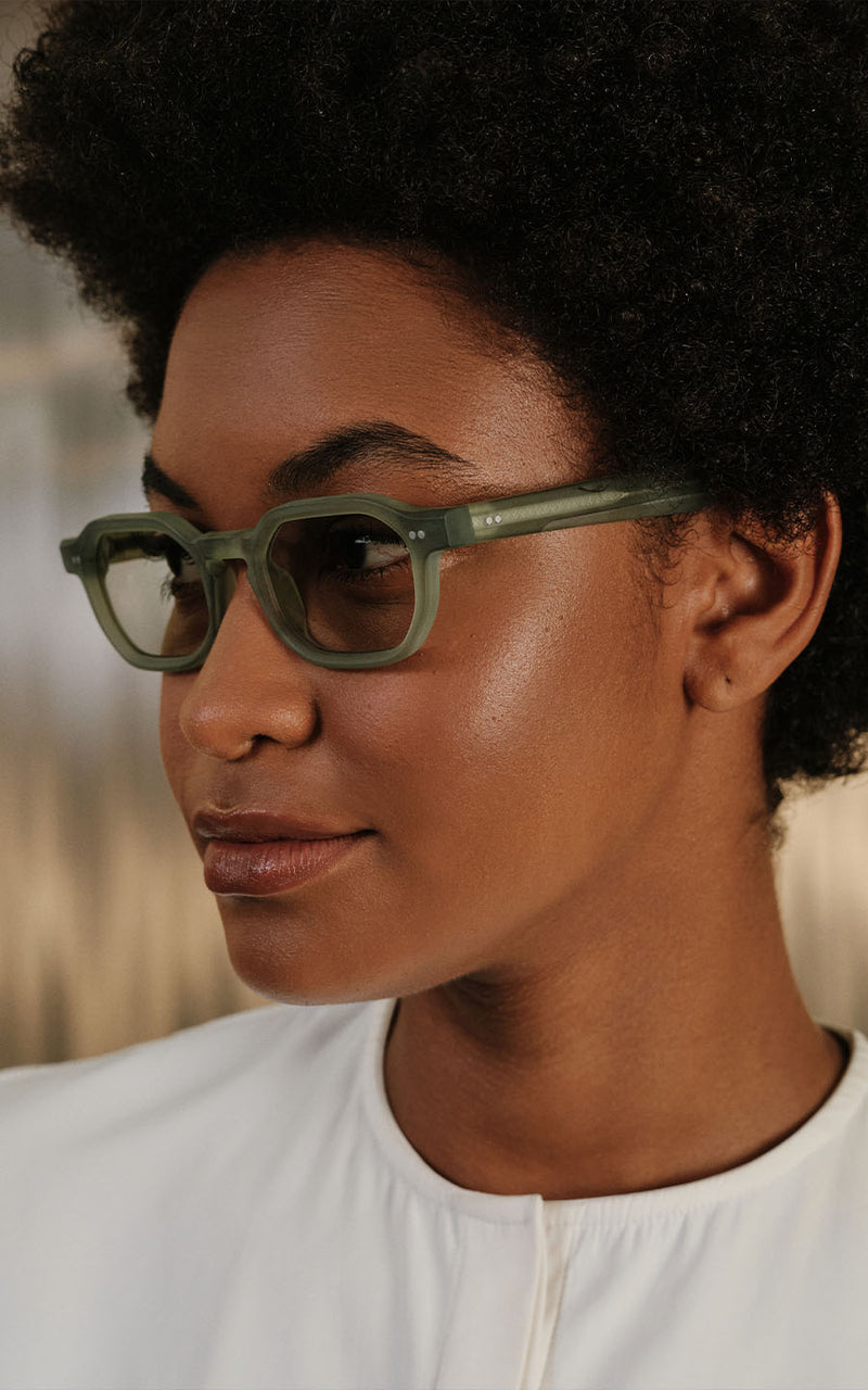 Mulher de perfil usa óculos de grau com armação verde translúcida e blusa branca