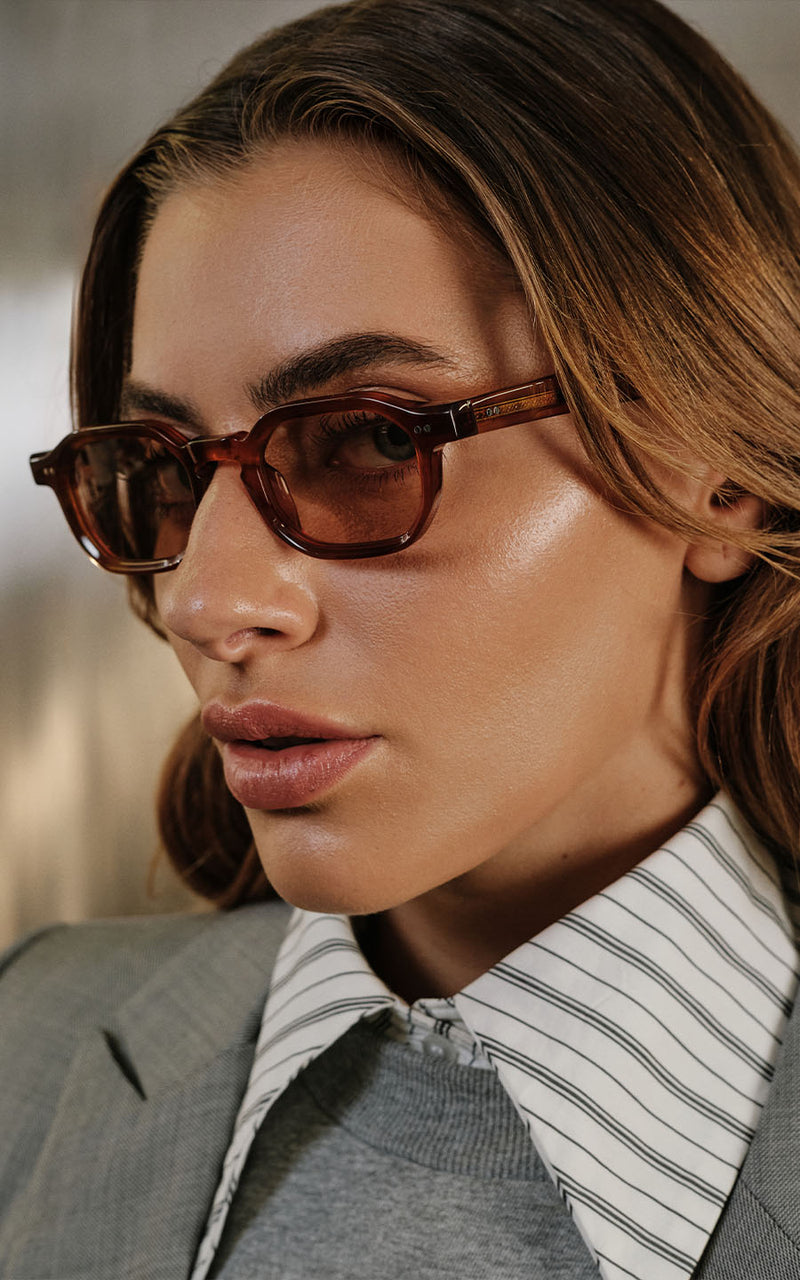 Mulher usando óculos de sol com armação geométrica marrom e camisa listrada