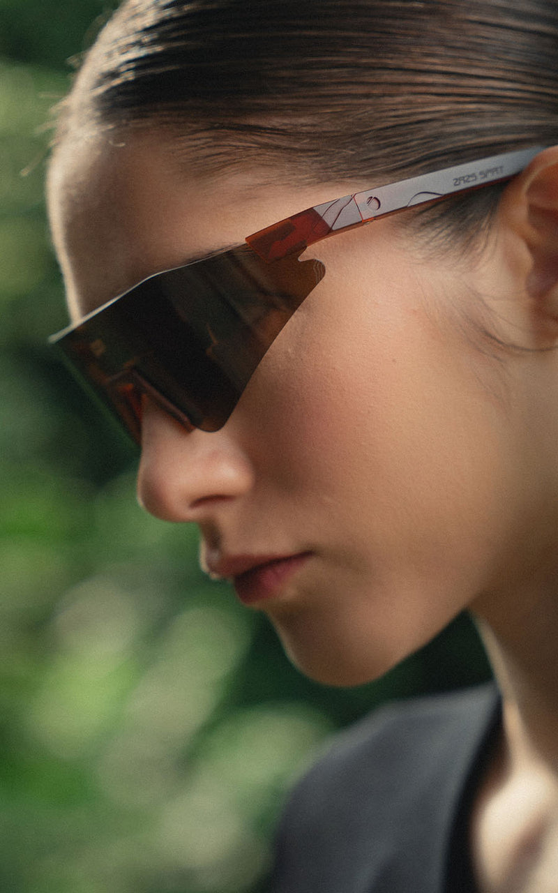 Mulher com óculos de sol esportivos com lentes escuras em ambiente externo verde 