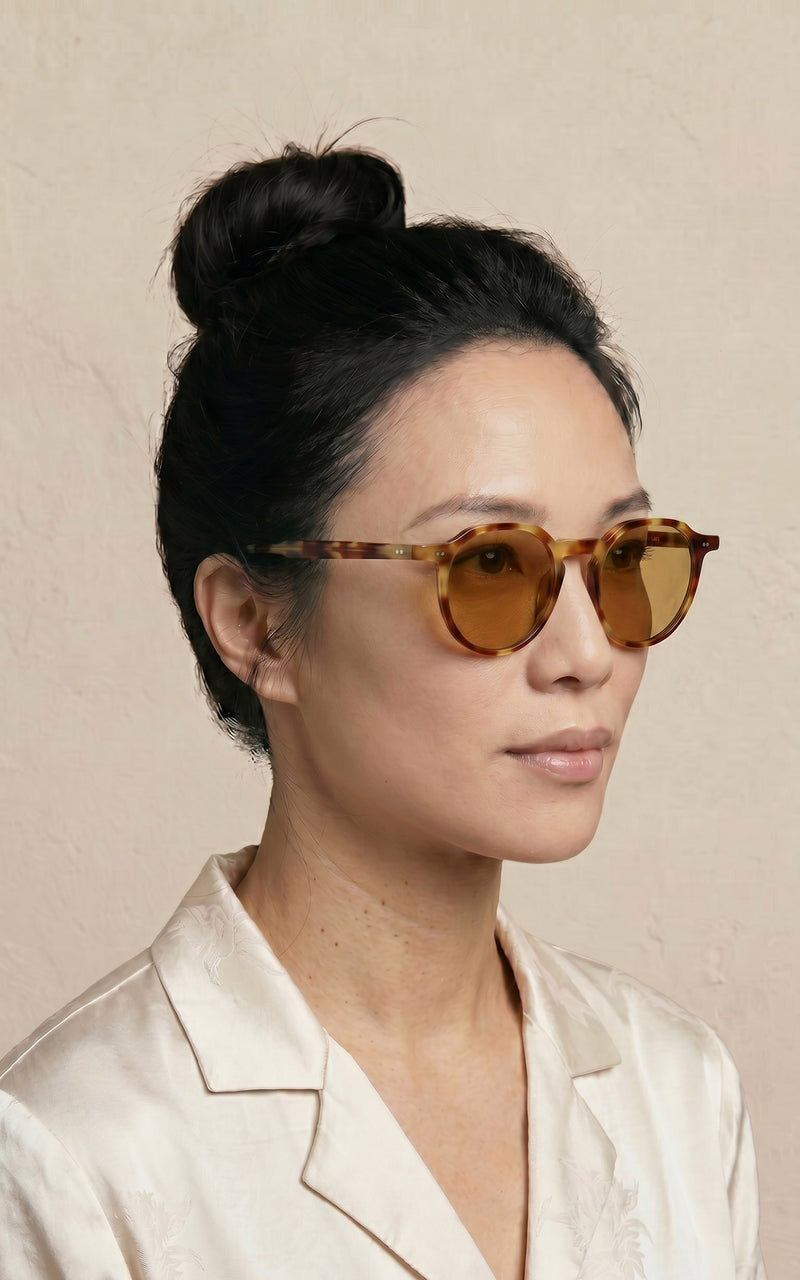 Mulher de perfil, vestindo blusa branca e óculos de sol com lentes âmbar