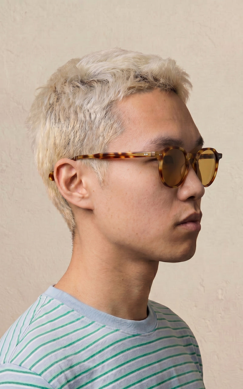 Homem de perfil usando óculos de sol com lentes marrons e camisa listrada 