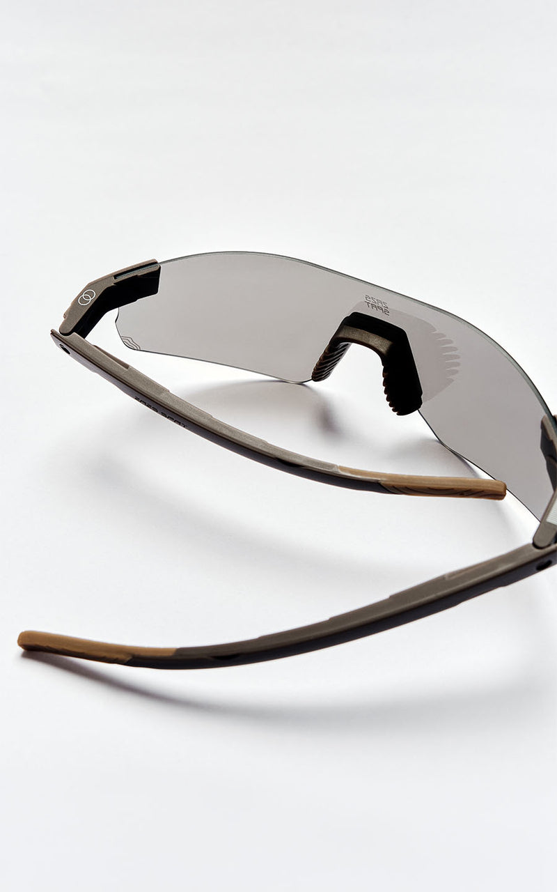 Óculos de sol esportivos com lentes cinzas e hastes marrons em fundo branco