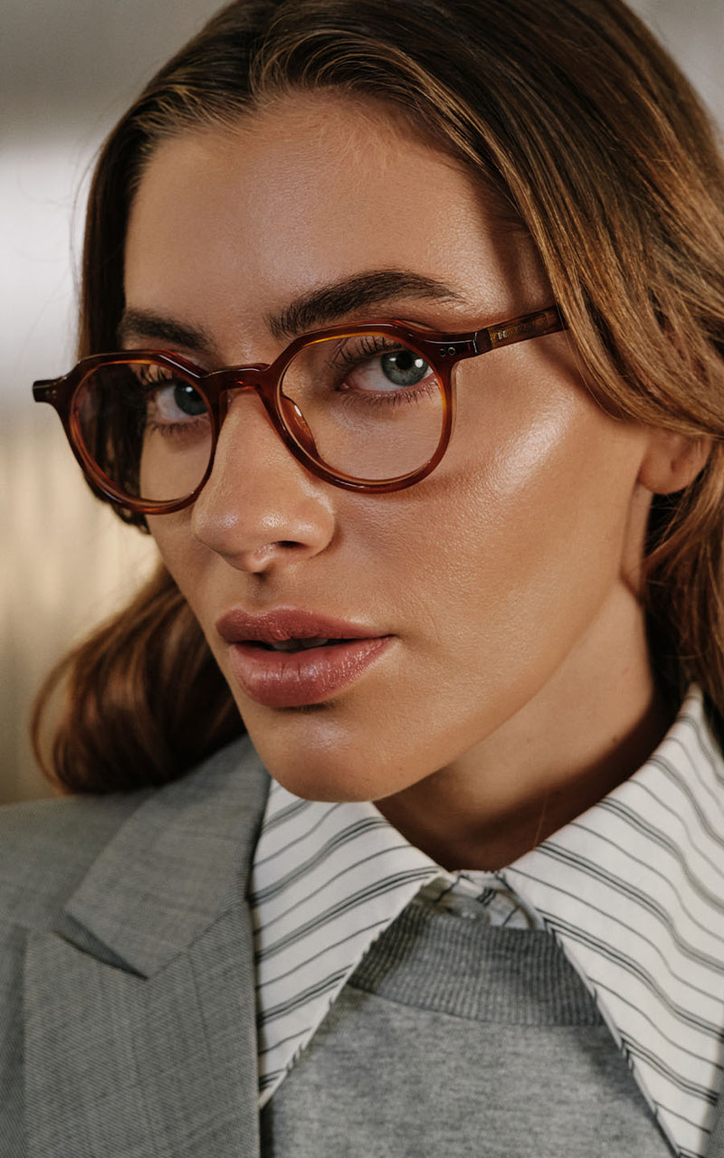 Mulher usando óculos de grau com armação marrom, camisa listrada e blazer cinza