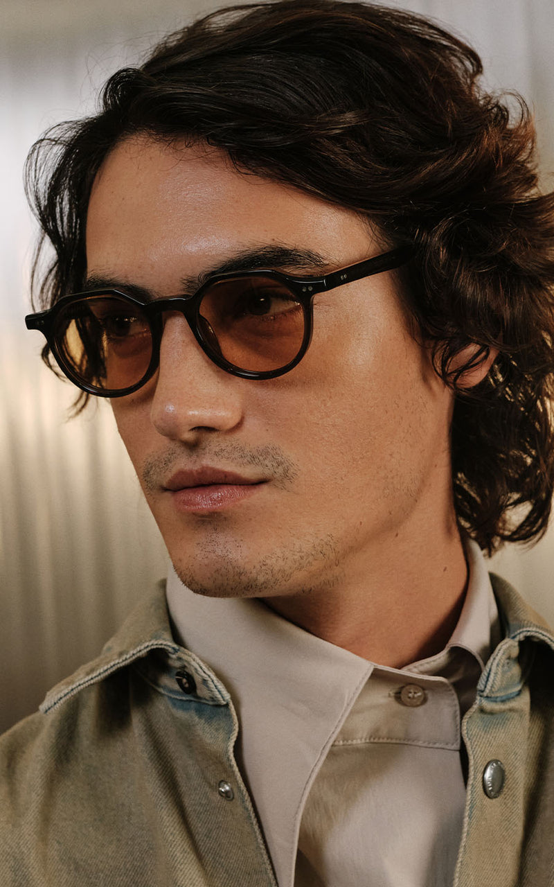 Homem usando óculos de sol com armação preta e lentes amareladas 