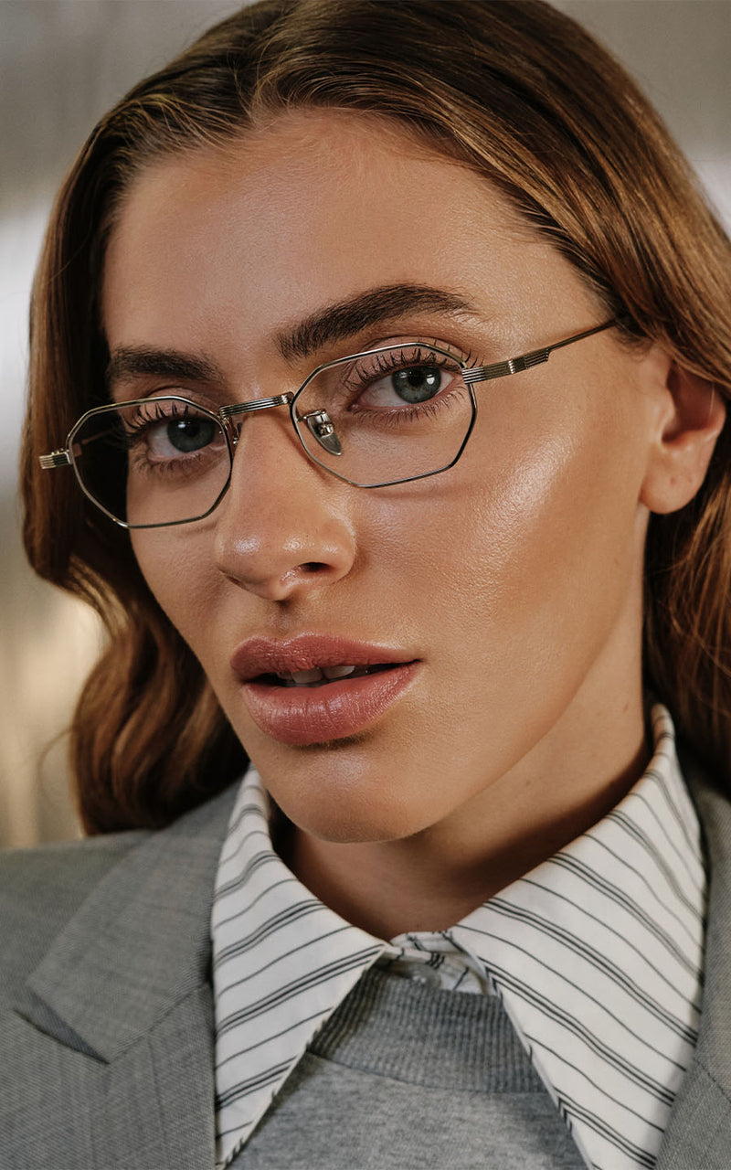 Mulher usando óculos de grau com armação metálica geométrica e blazer cinza