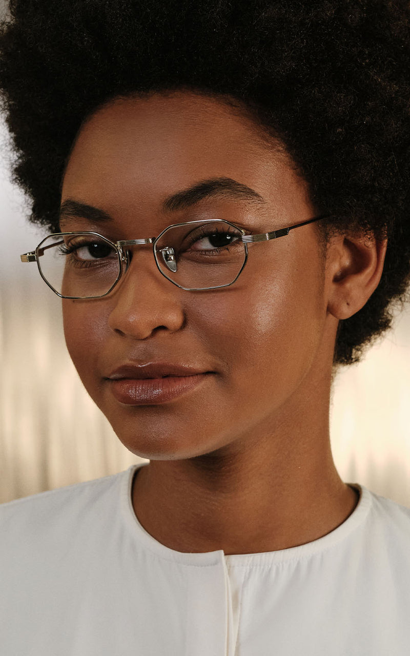 Mulher usando óculos de grau com armação metálica geométrica e blusa branca