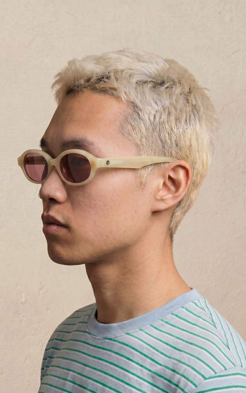 Homem de perfil , usando óculos de sol com armação clara e lentes rosadas 