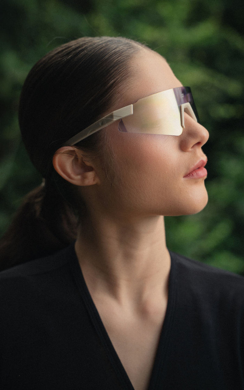 Mulher de perfil usando óculos de sol esportivos com lente espelhada e armação clara