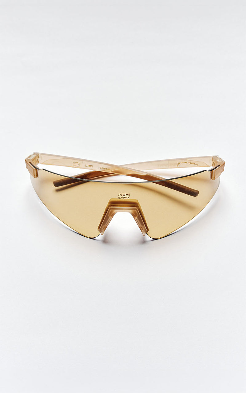 Óculos de sol esportivos com lentes em tom âmbar e hastes translúcidas sobre fundo branco 