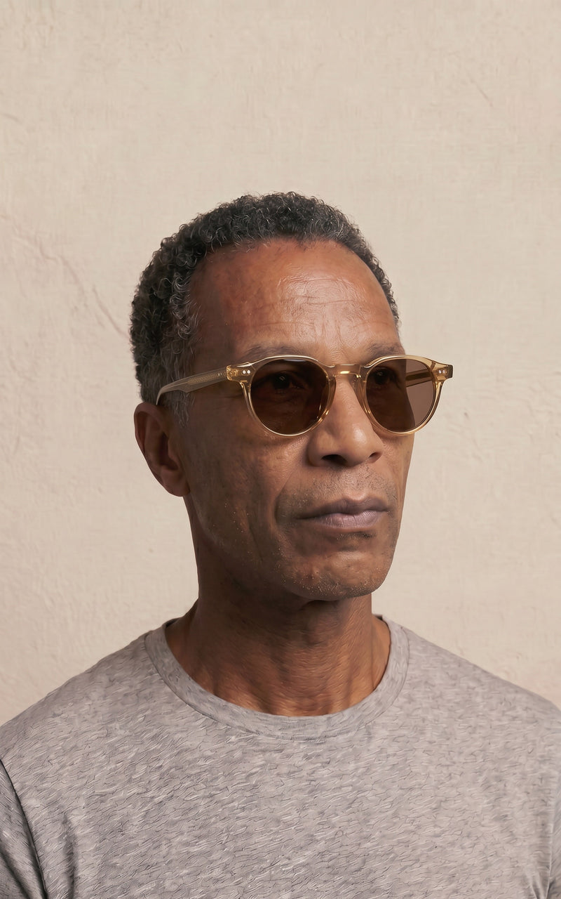 Homem usando óculos de sol com armação transparente e lentes escuras em fundo neutro