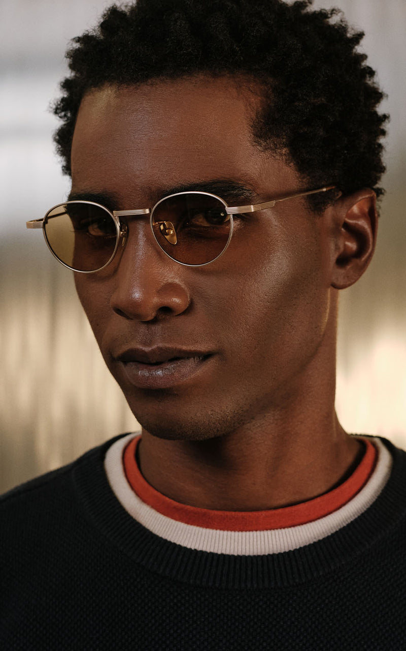 Homem usando óculos de sol com armação dourada e lentes levemente escurecidas 