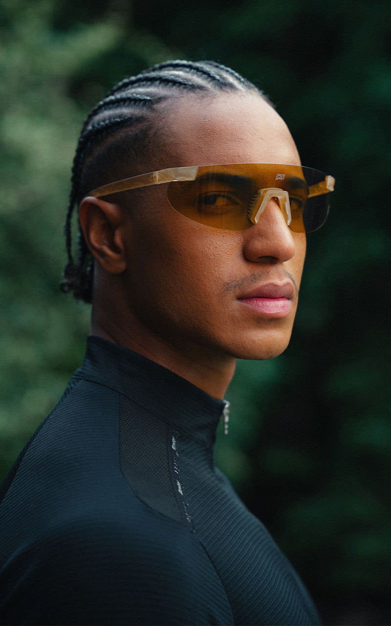 Homem vestindo blusa preta e óculos esportivos com lentes amareladas ao ar livre 