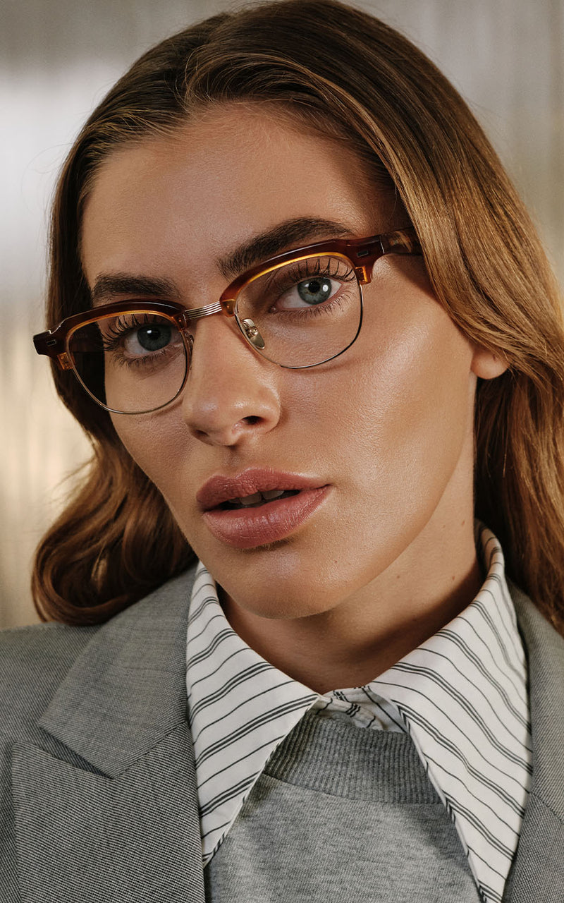 Mulher com óculos de grau com armação marrom, camisa listrada e blazer cinza