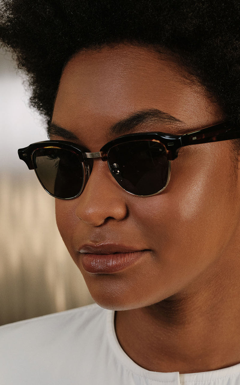 Mulher usando óculos de sol com armação preta estilo clubmaster e lentes escuras