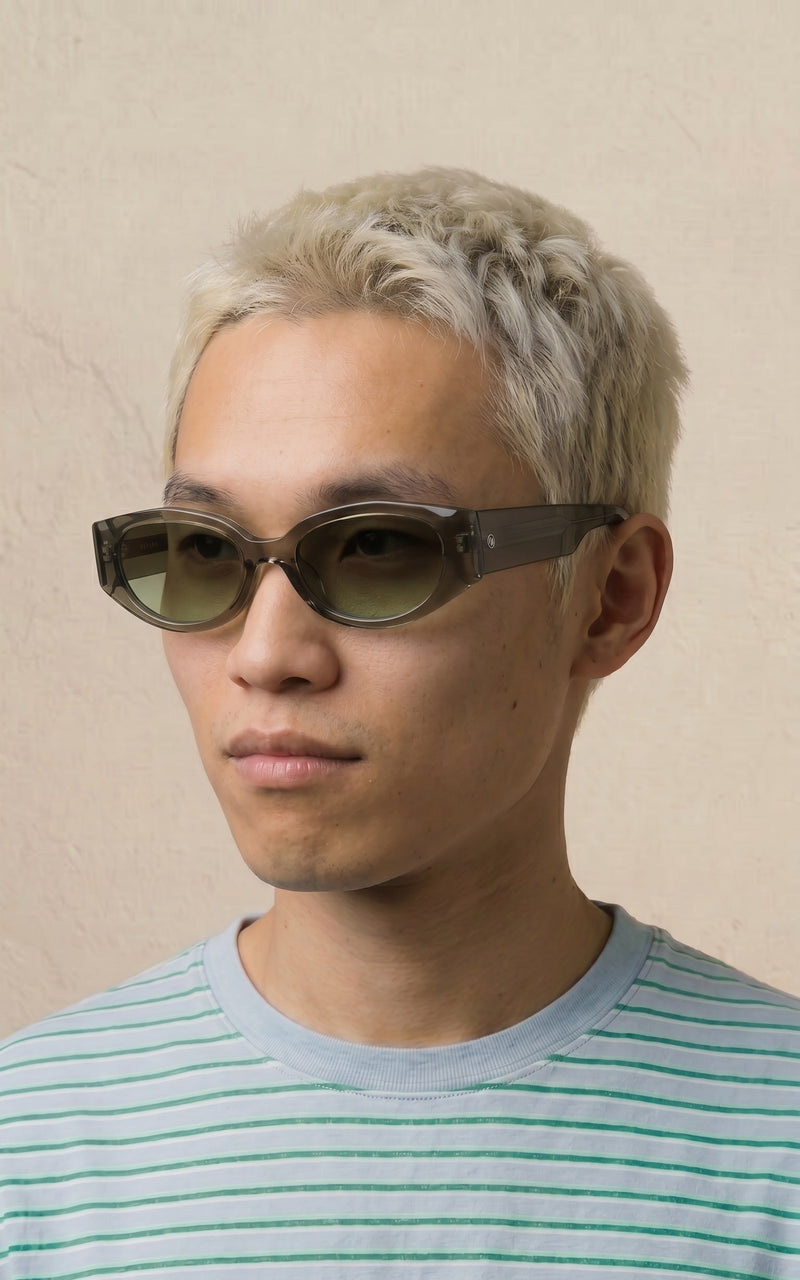 Homem usando óculos de sol com armação cinza transparente e lentes esverdeadas 
