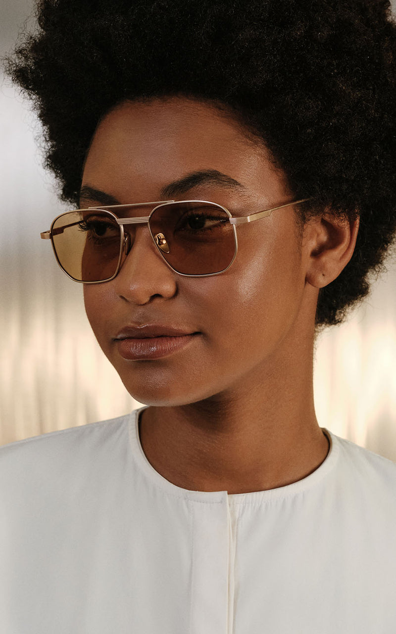 Mulher usando óculos de sol com armação dourada e lentes âmbar 