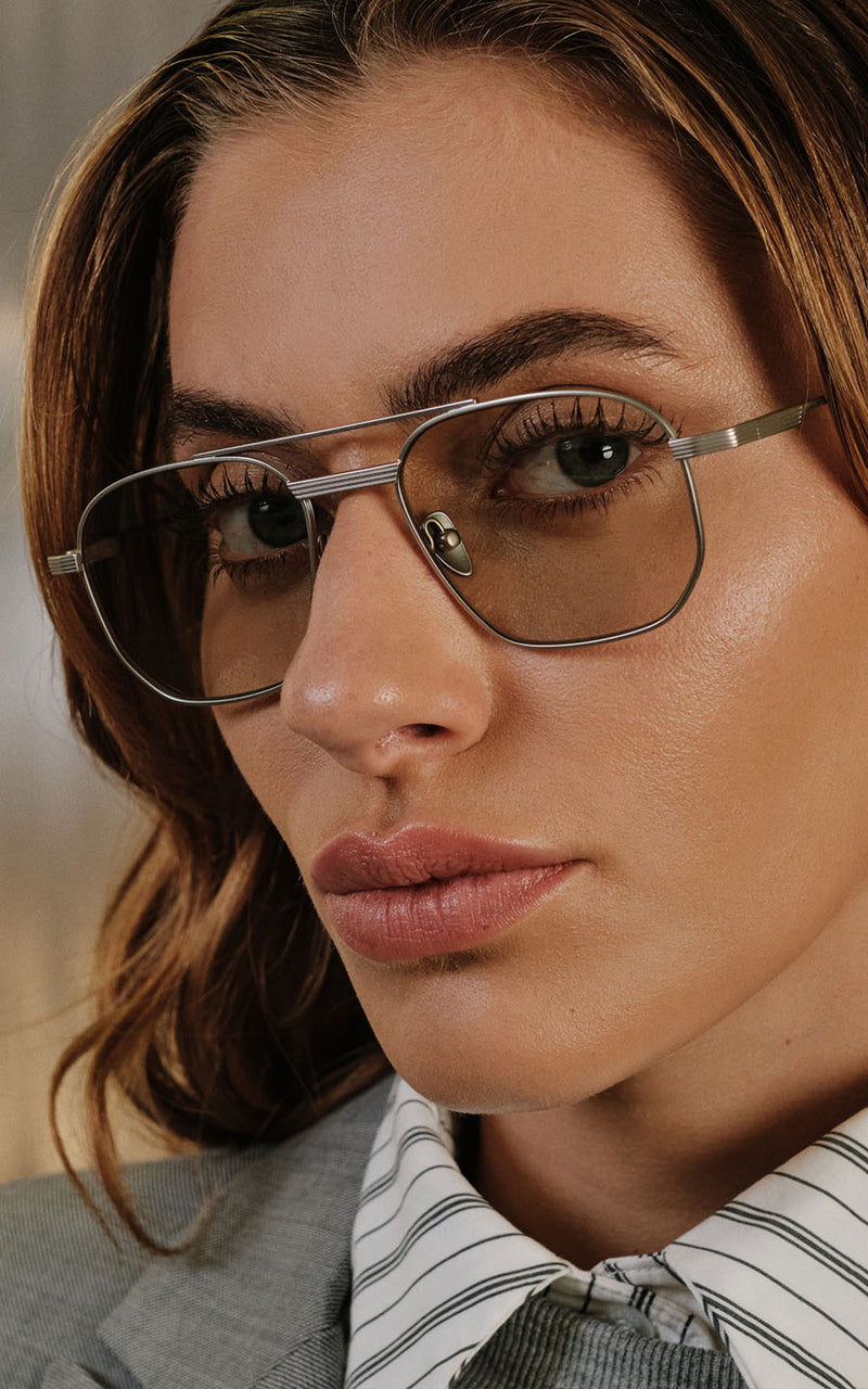 Mulher usando óculos de grau com armação metálica prateada e lentes levemente fumês 