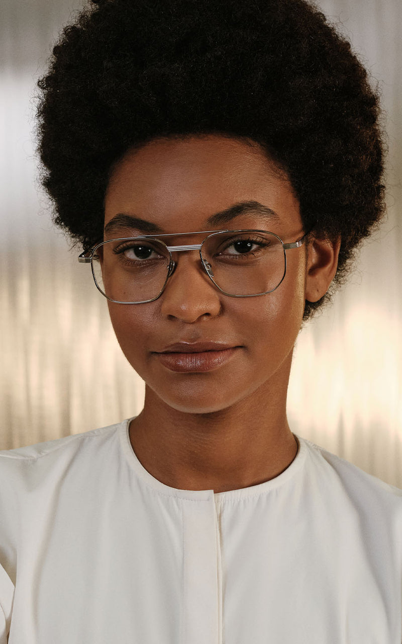 Mulher usando óculos de grau com armação metálica geométrica e blusa branca 