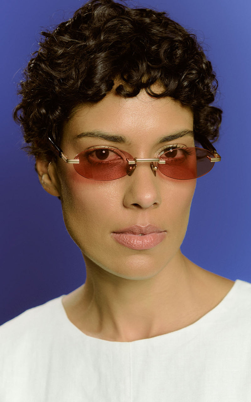 Mulher usando óculos de sol com lentes avermelhadas e armação dourada