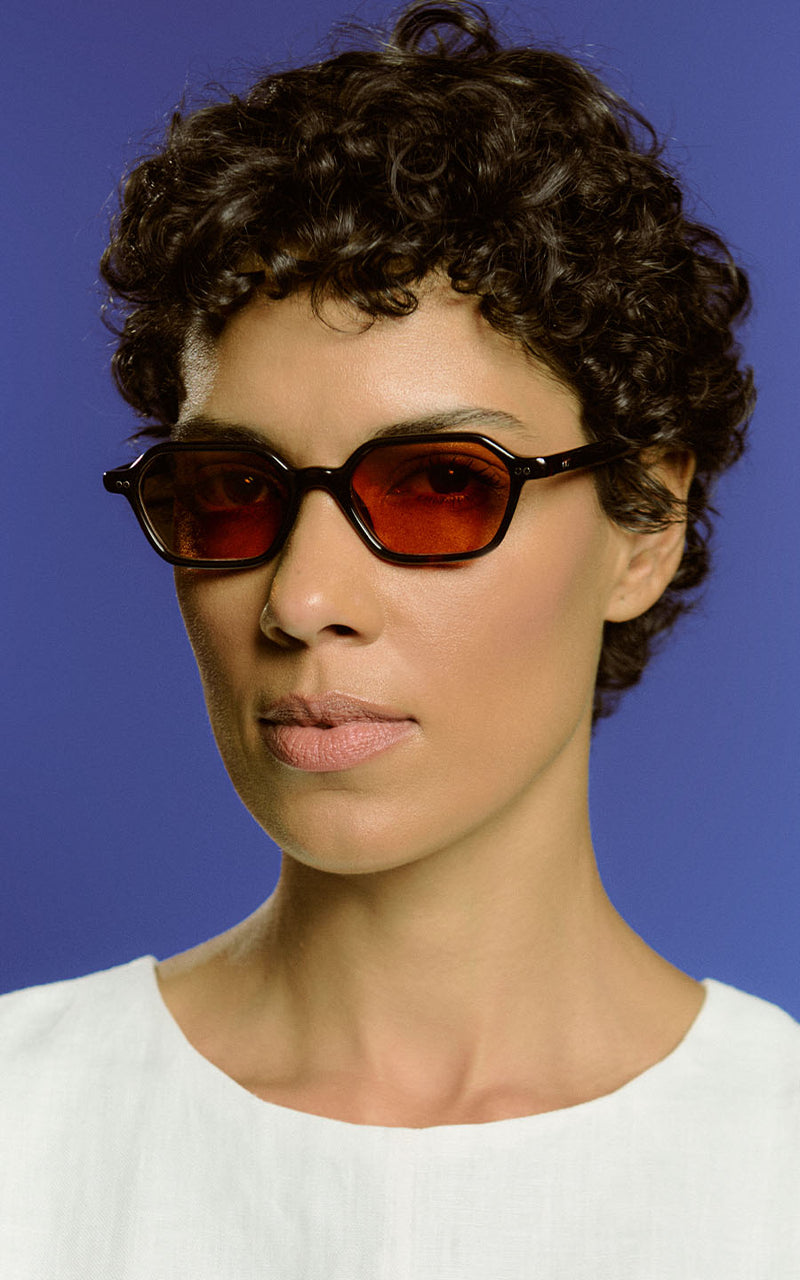 Mulher usando óculos de sol pretos com lentes avermelhadas contra fundo azul