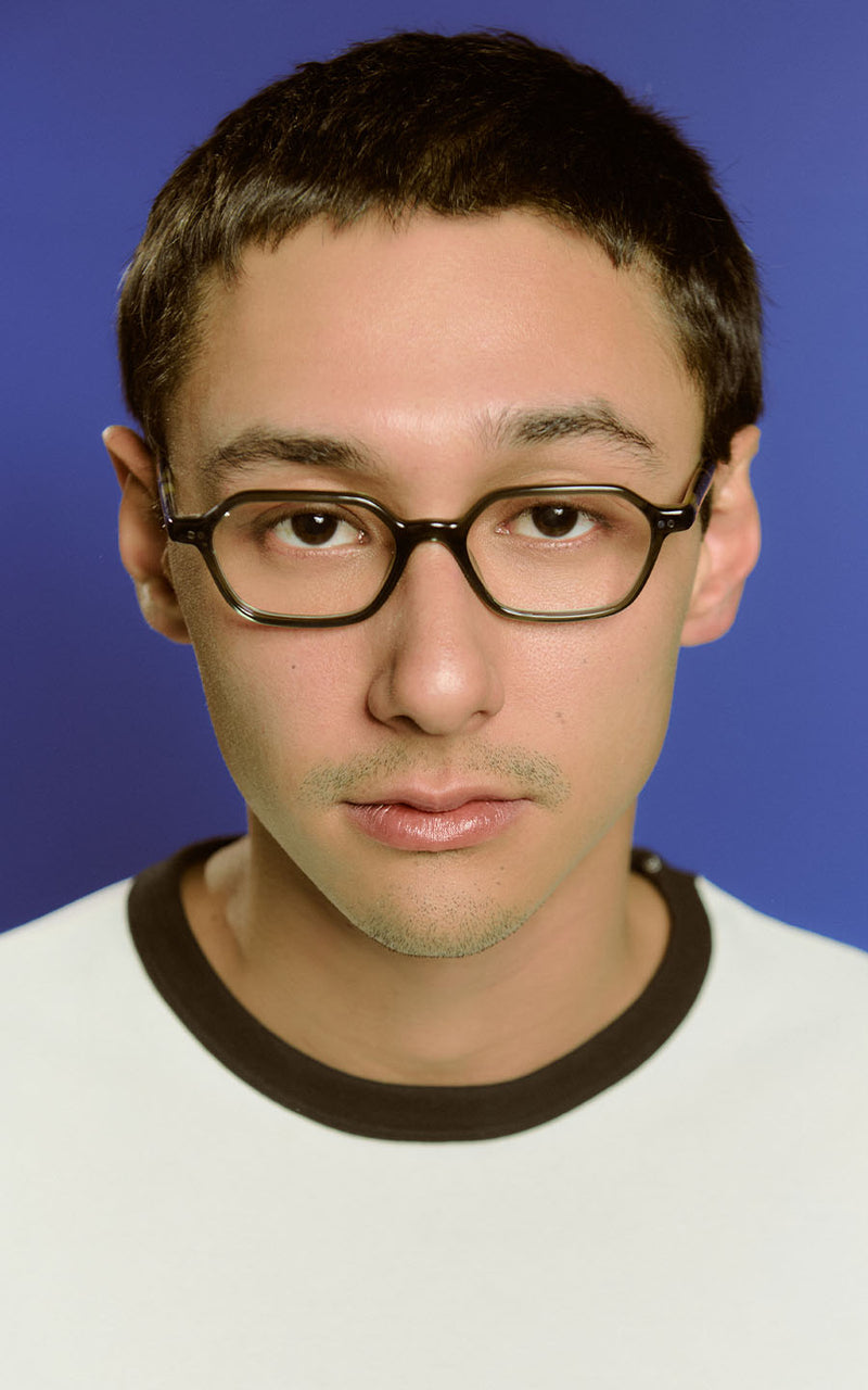 Retrato de um jovem de óculos com armação escura e camisa branca contra fundo azul