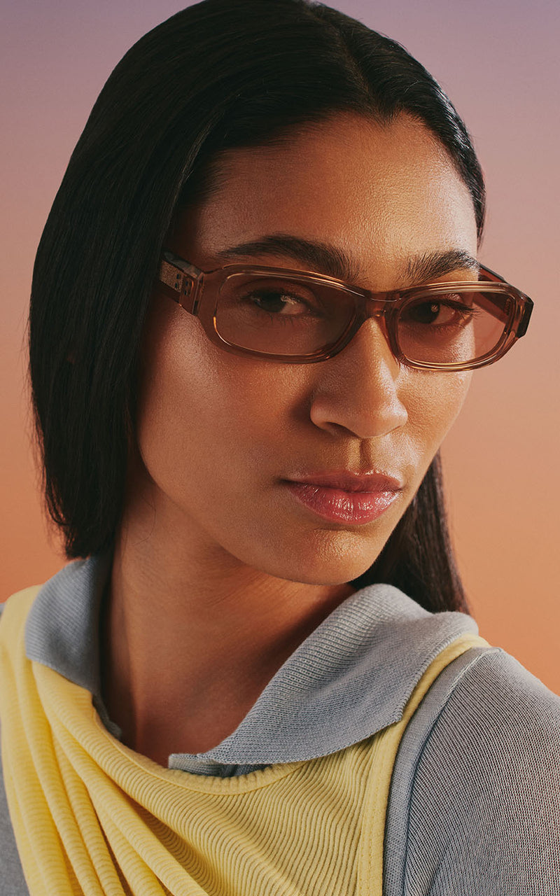 Mulher usando óculos de sol com armação marrom sobre fundo em tom pastel