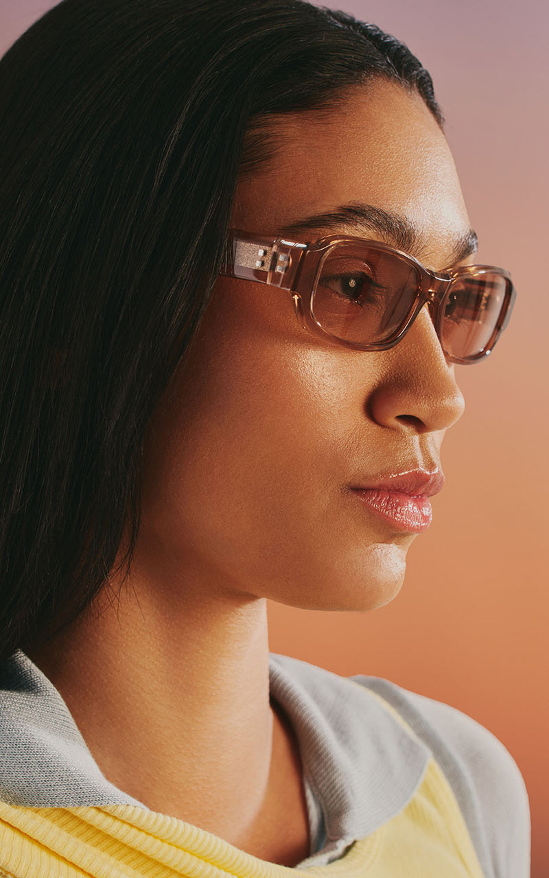 Mulher usando óculos de sol com armação translúcida e lentes rosadas em perfil 
