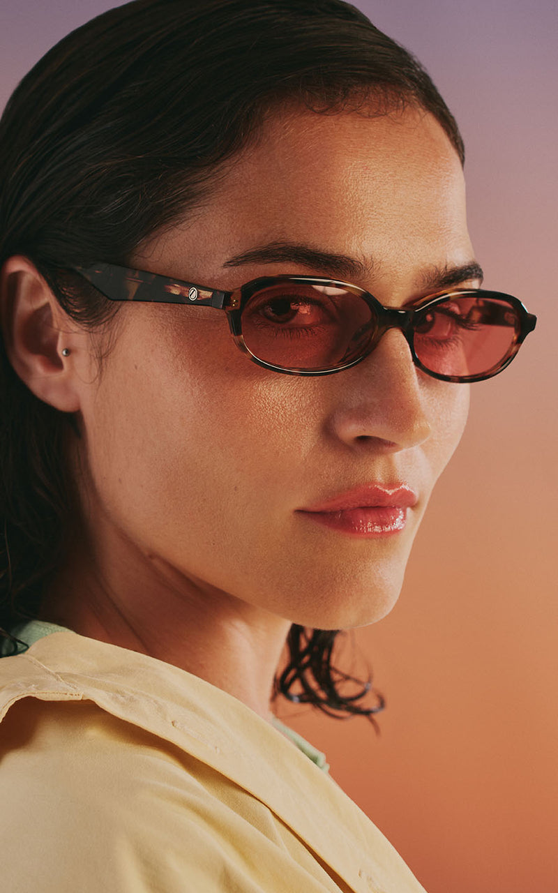 Mulher com óculos de sol e lentes rosadas contra fundo degradê