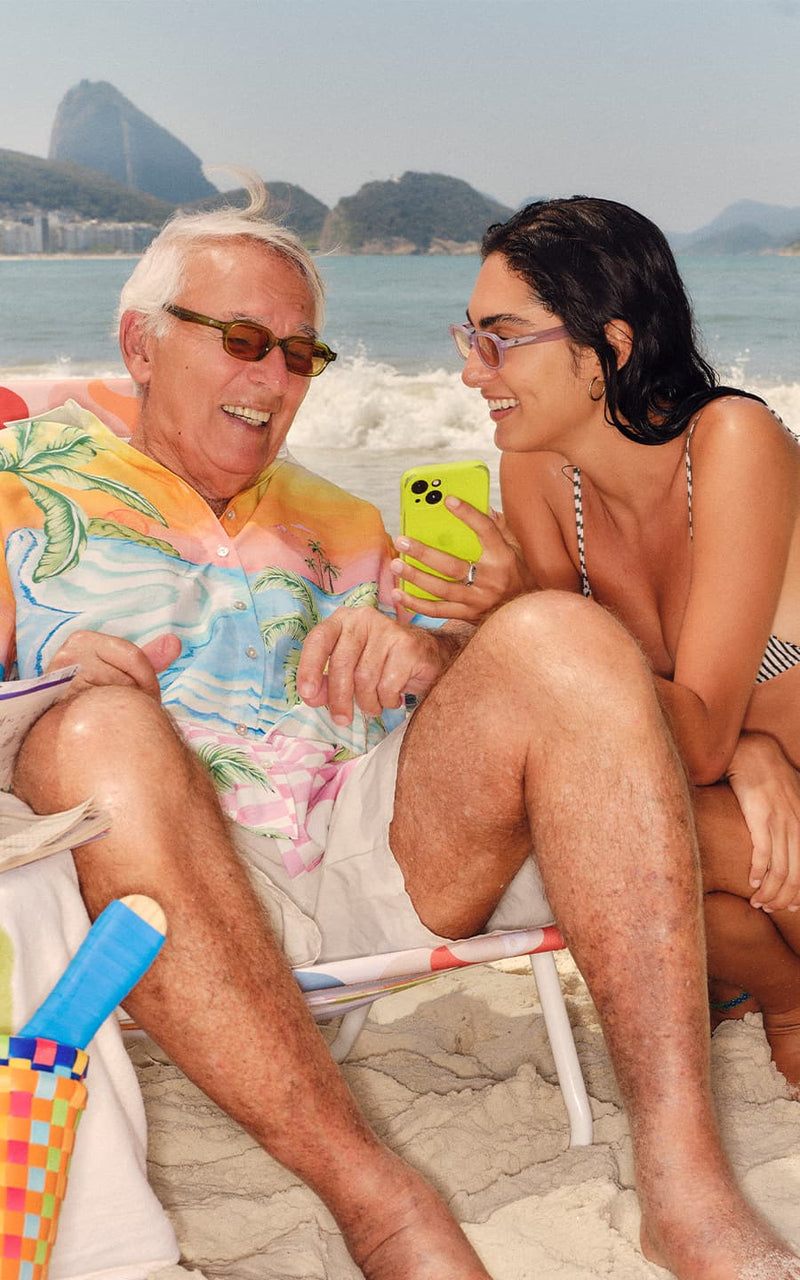 Homem sorridente de camisa florida conversando com uma jovem na praia 