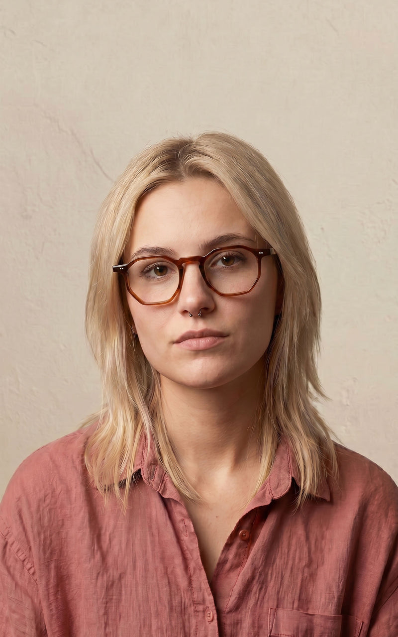 Mulher usando óculos de armação marrom hexagonal e camisa rosa claro